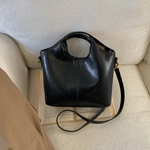 Detail of black matte leather bucket bag featuring circular handle and vertical stitching
