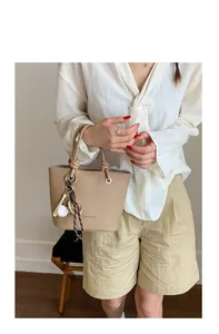 Detail of beige litchi grain leather tote bag with a unique baseball theme charm pendant