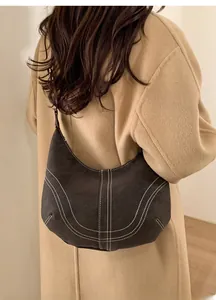 Detail of vintage dark brown suede half-moon bag with contrast white stitching on a model
