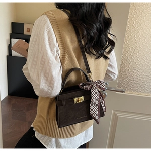 Detail of dark brown leather handbag with gold metal lock and silk scarf on handle