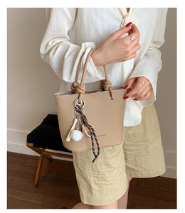 Detail of khaki litchi grain bucket bag with knotted handle and sports charm accessory