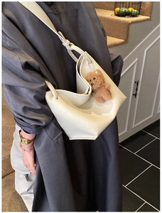Détail du sac seau en cuir blanc cassé avec un charm ours en peluche marron sur un modèle