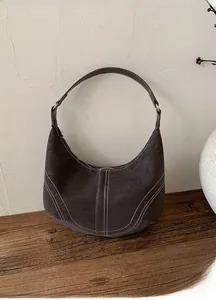 Detail of dark brown vintage dumpling bag with contrast stitching on wooden surface