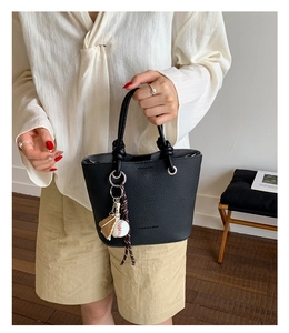 Detail of black lychee leather bucket bag with baseball charms on a fashion model