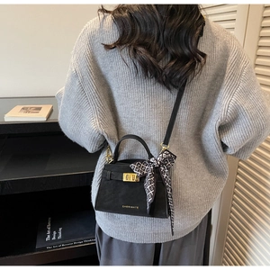 Detail of a black crossbody bag with silk scarf on handle shown on a model's back