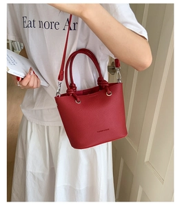 Detail view of red lychee pattern bucket bag featuring gold metal rings and leather straps