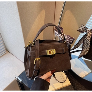 Detailed close-up of dark brown suede handbag with gold lock and decorative silk scarf