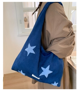 Detail of blue plush tote bag with star embroidery worn by model in indoor setting