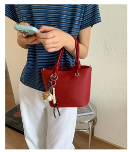Detail of red lychee pattern bucket bag with sports charms in minimalist home setting