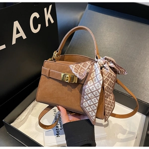 Close-up of brown faux leather trapezoid handbag with gold lock and silk scarf detail