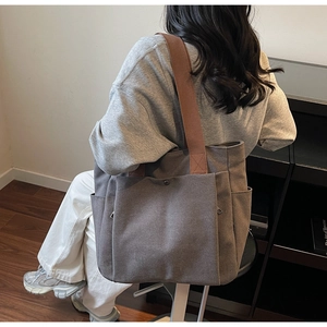 Detail of grey canvas tote bag with front snap pocket and brown shoulder strap on model