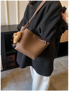 Détail d'un sac seau en cuir marron à motifs litchi avec surpiqûres et breloque ours