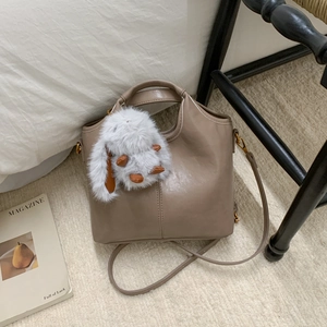 Detail of taupe leather bucket bag with cute white plush rabbit charm on a cozy bed