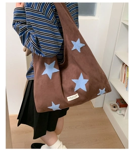 Brown plush tote bag with blue star embroidery worn by model in a home setting