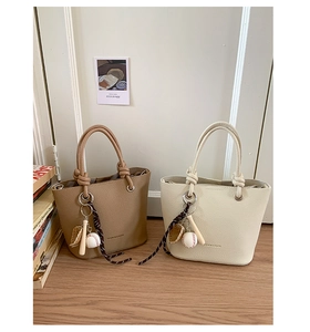 Detail of lychee textured bucket bags in khaki and cream with baseball-themed charms
