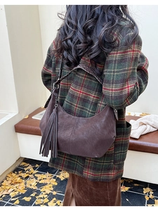 Detail of dark brown hobo bag with long fringe charm and studded strap in autumn setting
