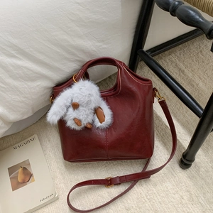 Detail view of burgundy leather bucket bag with white plush bunny charm and strap