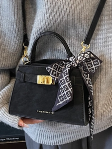 Elegant black suede handbag with gold lock and printed scarf worn with knit sweater
