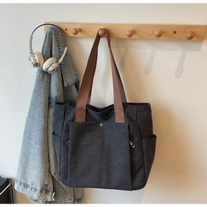 Détail d'un sac cabas en toile noire avec lanières brunes et fermeture éclair argentée