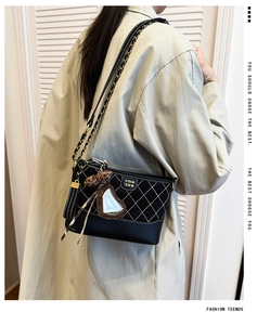 Detailed view of black quilted crossbody bag with metal chain strap and plush bear charm
