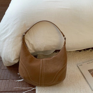 Close-up of brown leather crescent bag featuring distinct white contrast stitching details