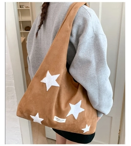 Detailed side view of a large brown faux suede tote bag featuring star patches on a model
