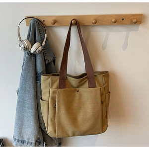 Détail de cabas en toile avec poche avant à bouton métallique et anses marron foncé