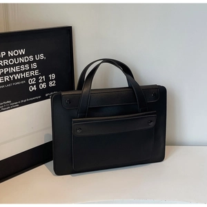 Detail of minimalist black faux leather tote bag showing the snap button front pocket