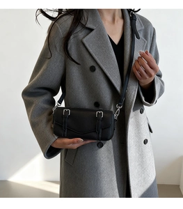 Detail shot of a black textured leather crossbody bag with buckle straps on a grey coat