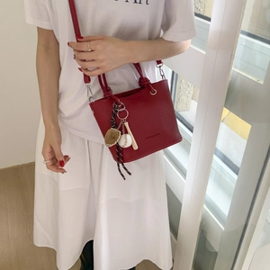 Red lychee texture bucket bag with dual handles and baseball keychain on a model