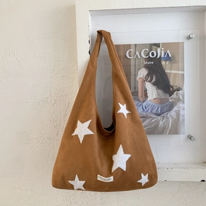 Detail of brown hobo bag with star appliques and small woven label on textured wall