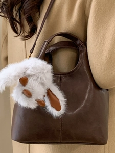 Brown leather bucket bag with plush rabbit charm and adjustable strap for winter fashion