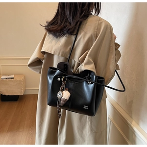 Detail view of black leather tote bag with plush charm on khaki trench coat model