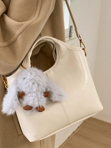 Creamy white leather bucket bag with plush rabbit charm and gold buckle on camel coat