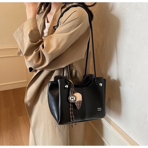 Detail view of black leather tote bag with unique checkered charm on casual trench coat