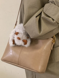 Beige leather bucket bag with gold buckle and plush charm, styled as shoulder handbag