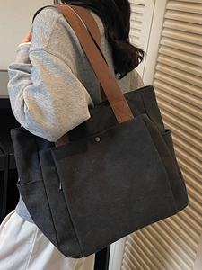 Sac fourre-tout minimaliste en toile noire avec anses brunes vu d'un angle latéral chic