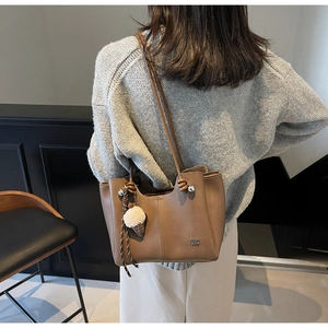 Brown leather tote bag detail with plush ice cream charm and silver logo on shoulder