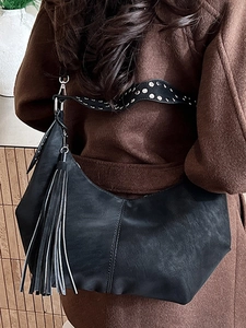 Chic black underarm bag with fringe tassel and silver studded wide strap on woman coat