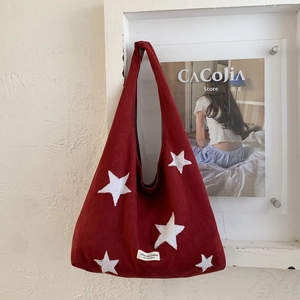 Detailed view of red plush tote bag with white star embroidery hanging on a textured wall