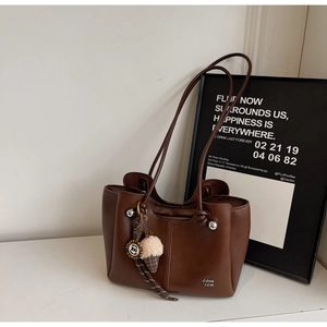 Detail view of a dark brown leather tote with a plush ice cream charm and metal rivets