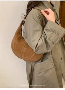 Side view of a brown leather crescent shoulder bag with white contrast stitching detail
