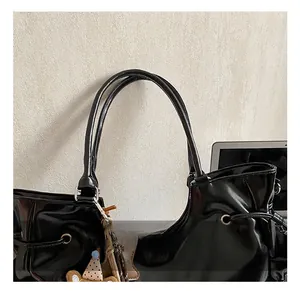 Détail d'un sac à bandoulière noir brillant avec doubles poignées et pendentif ours
