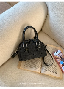 Close-up of black bow-print woven shell bag featuring metal studs on a cream sofa
