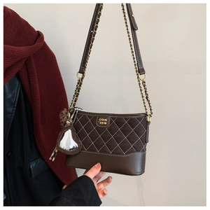 Detail of a brown quilted hobo bag featuring a heart mirror charm and metal chain strap