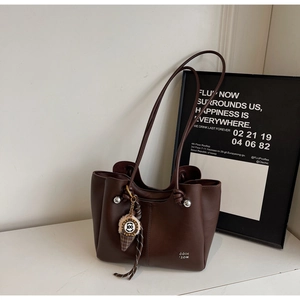 Detail view of coffee brown tote bag with silver studs and ice cream charm on white surface