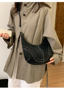 Detail view of black suede crescent bag with white contrast stitching and silver hardware
