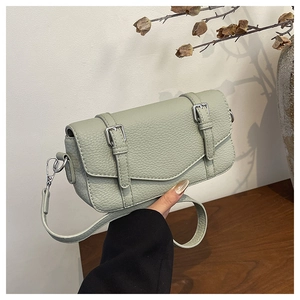 Detail of light green litchi texture leather handbag with silver buckles held in hand