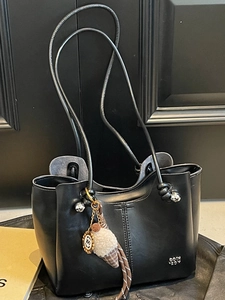 Minimalist black faux leather tote bag with knotted shoulder straps and plush pendant charm