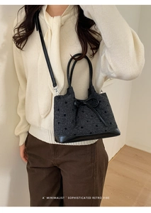 Détail d'un sac seau en tweed gris à pois avec un nœud en cuir noir et une poignée élégante